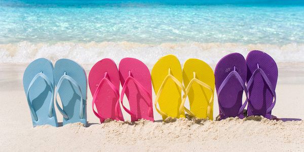 Imagem ilustrativa: chinelos de dedo coloridos expostos em uma praia, sem marca aparente