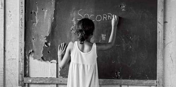 Foto em preto e branco: aluna escreve "socorro" na lousa